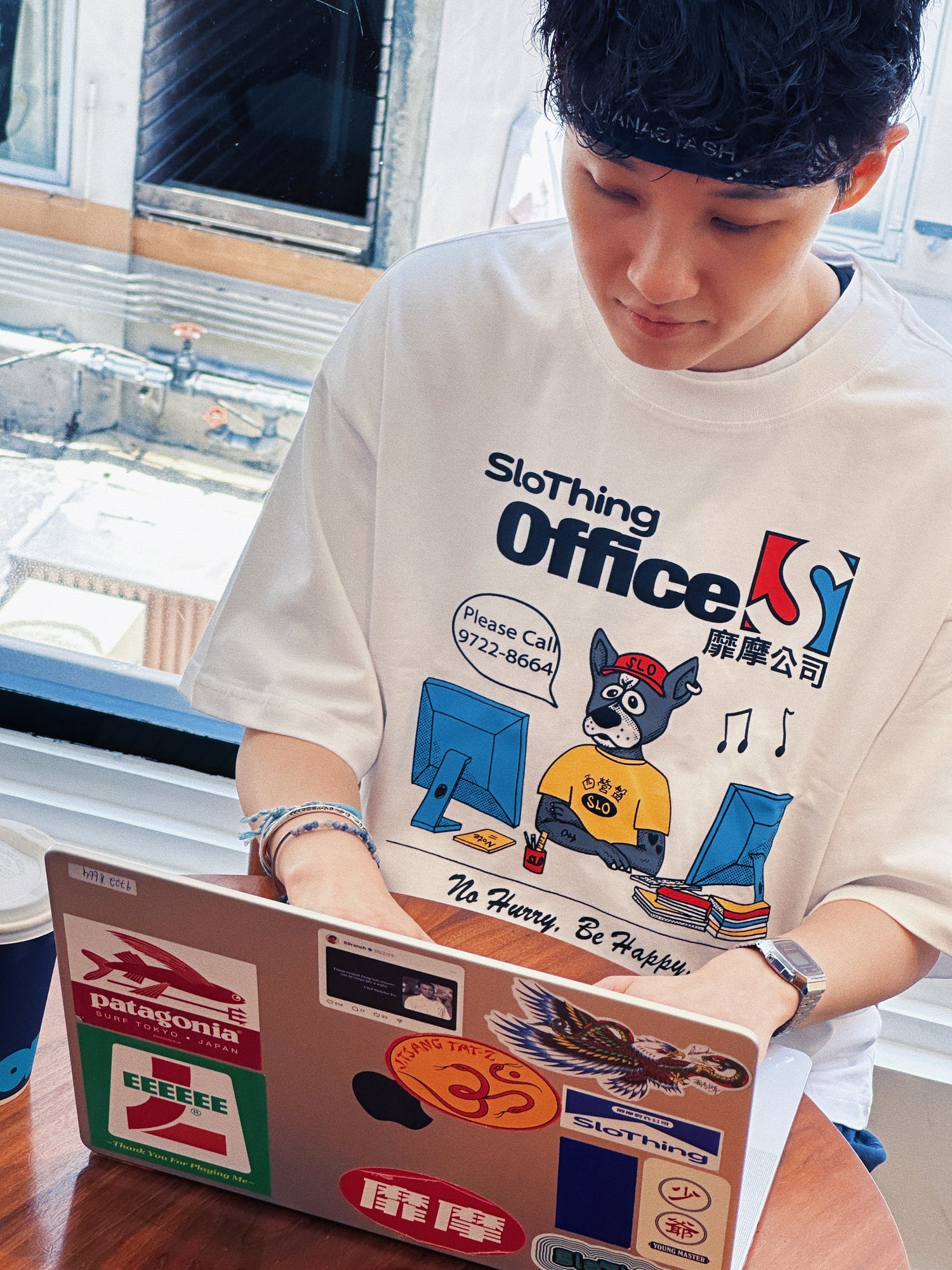 Person wearing a white t-shirt with a graphic design, using a laptop with stickers.