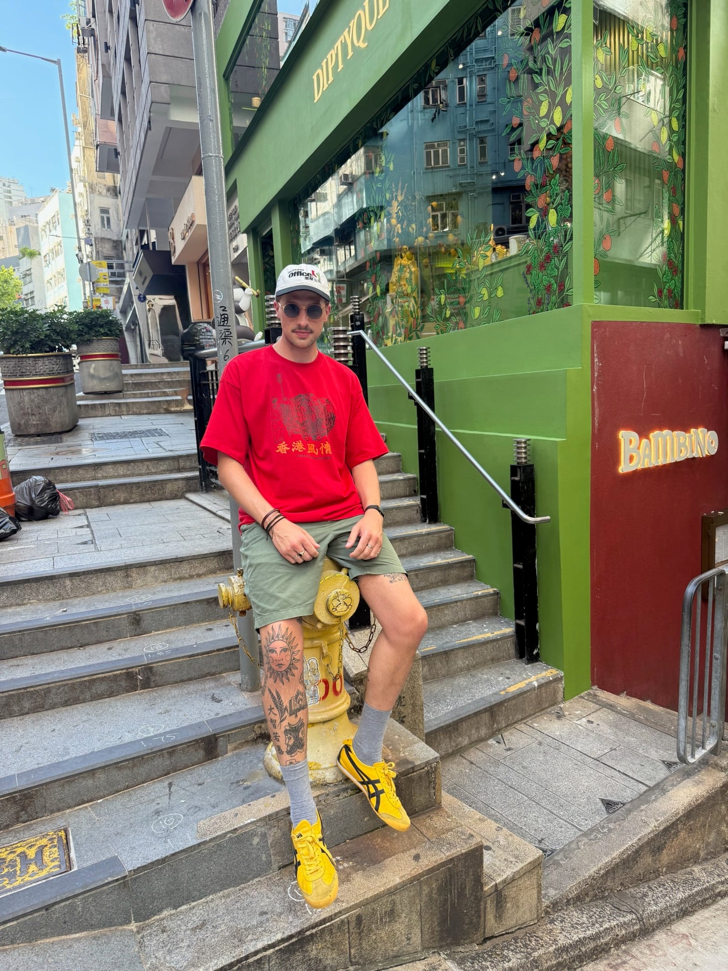 Person in red shirt and yellow shoes standing on a staircase with a green building in the background